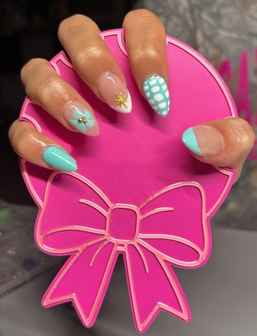 Almond nails in sheer nude and teal with a bow, a gold star charm, and white dots, by Leighton
